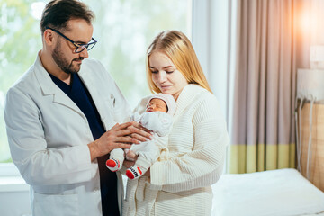 Male pediatrician nurse taking care of newborn baby at hospital ward. A doctor or male midwife visiting mother after birth or cesarian holding a new born baby in her arms at the hospital room. - obrazy, fototapety, plakaty
