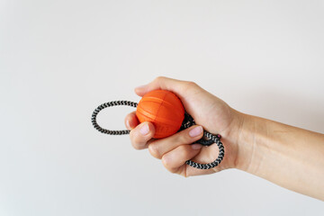 A hand holds a small orange basketball with a black and white rope attached to it, a toy for a dog.