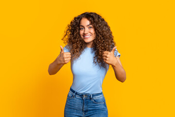 Happy curly woman giving two thumbs up on yellow