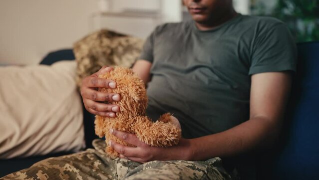 Pensive African American military holding teddy bear, missing his little child