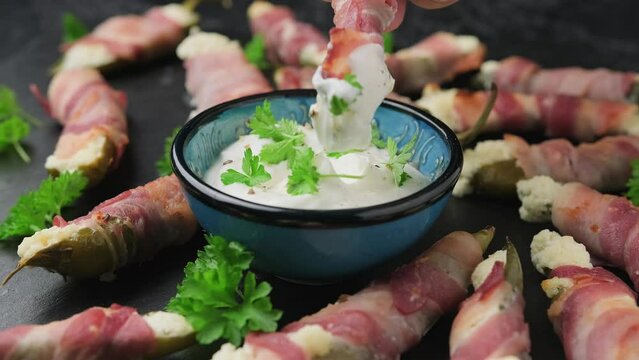 Dipping Bacon Wrapped Jalapeno Poppers in greek yogurt sauce