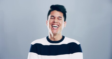 Comic, face and man laughing in a studio for funny or silly joke in conversation with happiness. Smile, portrait and young Asian male model with goofy facial expression isolated by gray background.