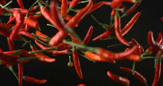 Super slow motion macro of fresh bio organic red hot spicy chili peppers are flying at 1000 fps isolated on dark background.