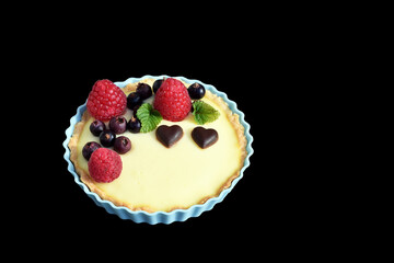 Shortbread vanilla tartlet with fruits, two chocolate hearts and lemon balm leaves. Isolated on black background