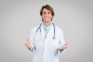 Portrait of happy european man doctor in workwear with stethoscope on neck gesturing and talking at camera