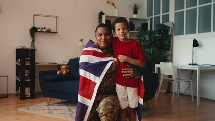 Portrait of proud soldier father and little son wrapped in United Kingdom flag