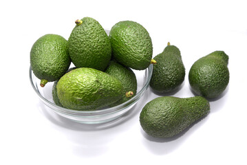 Glass bowl on white background filled with bright green avocados and also avocados on the table, fruit and healthy food.