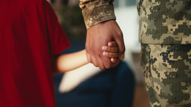 Little boy holds soldier father's hand, parent leaving for the military service