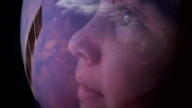 A teenage boy watches with admiration the planet earth from a space station wearing a spacesuit. Beautiful planet reflected in the glass of a space helmet. Astronomy and space exploration for children