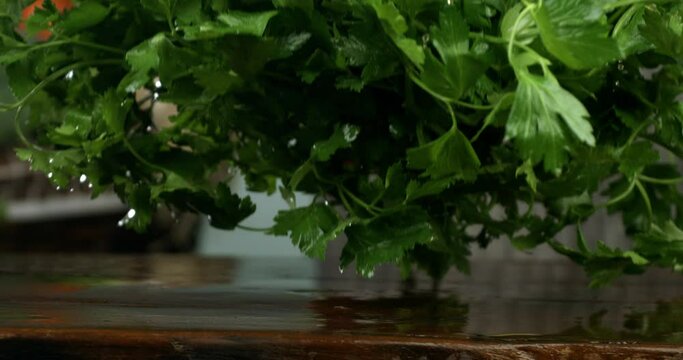 Super slow motion macro of falling fresh ripe organic parsley on rustic wooden cut board in kitchen of restaurant at 1000fps.