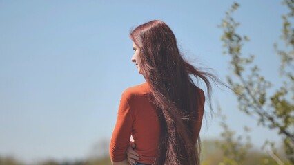 A girl with burgundy long hair admiring nature on a summer day.