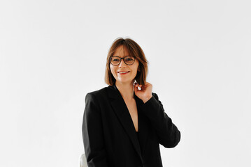 Positive smiling adult elegant woman in black suit and glasses posing, studio shot