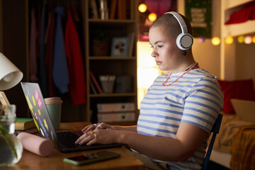 Side view portrait of bald young woman wearing headphones and using laptop while studying at night...