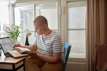 Side view portrait of bald young woman studying at home or in college dorm room and holding...
