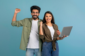 Excited young indian couple holding and using laptop