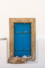 Traditional blue shutters and whitewashed walls on the side of an old greek building.