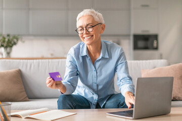 mature lady holding credit card sitting near laptop at home