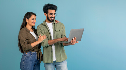 Indian couple using laptop together, blue studio background