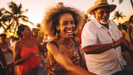 A joyful adult Hispanic woman in a bright dress dances at a beach party with an elderly man in a hat.