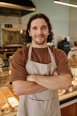 Bakery worker confidently standing against counter with arms crossed and looking at camera