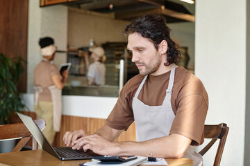 Eatery caucasian worker attentively looking through information on laptop screen sitting at table