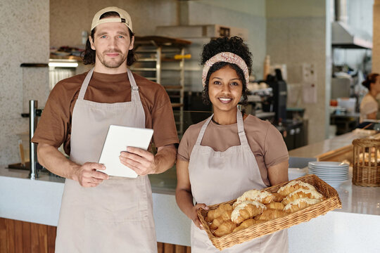 Medium shot of young biracial bakery workers standing against counter smiling at camera