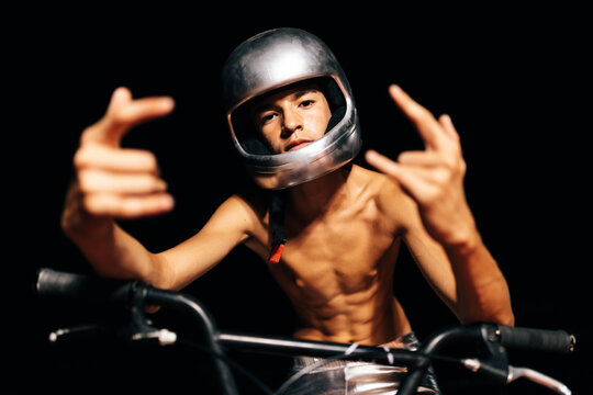 Unrecognizable young shirtless man sitting on bicycle in lights and showing devil horns gesture