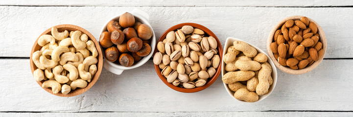Various kinds of dried nuts (almonds, pistachios, peanuts, hazelnuts and cashews) in bowls on white...