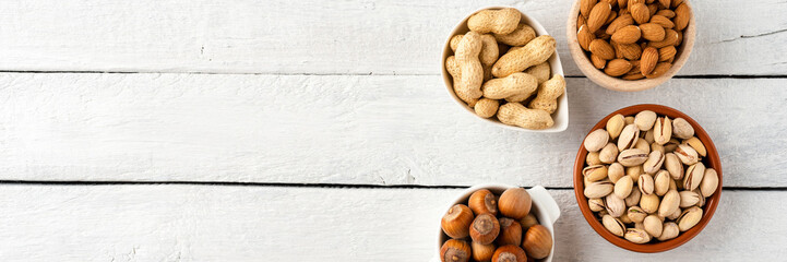 Nuts: almonds, pistachios, peanuts, hazelnuts and cashews in bowls on white wooden background with...