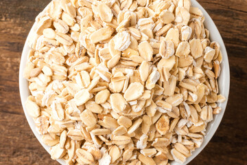 Rolled oats in bowl on rustic wooden table. Top view