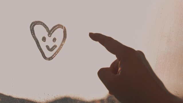 woman's finger painted doodle two hearts with smile face on foggy glass on pink window