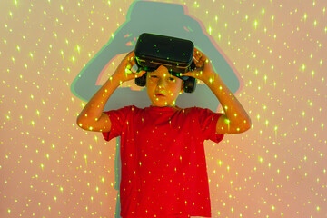 Cute boy in VR goggles standing in neon lights and looking at camera
