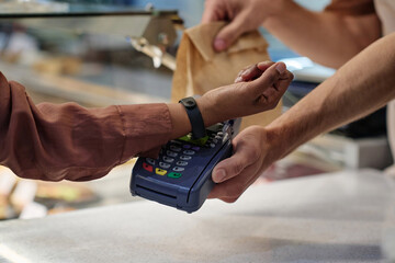 Unrecognizable woman paying with smartwatch for takeaway order, unknown cashier receiving payment