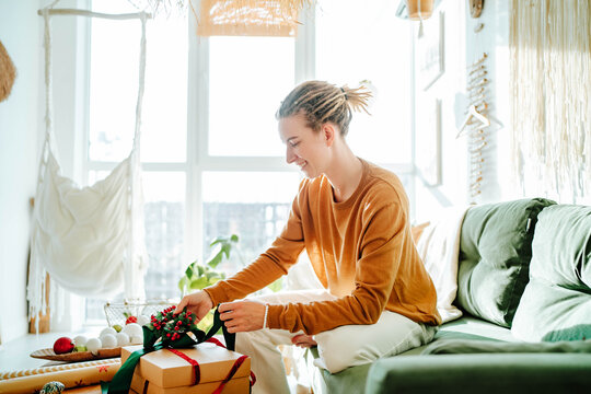 Side view if Young woman preparing present box at home while sitting on sofa