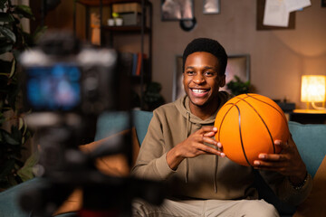 A basketball player sits in a tidy living room, ball in hand, dressed casually. He looks relaxed...
