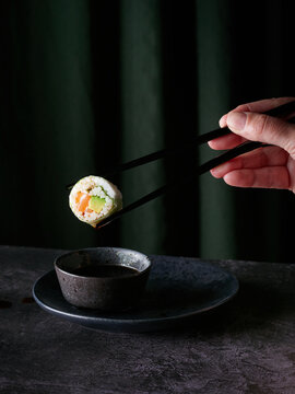 Sushi Roll in Chopsticks with Sauce Drip above bowl on table against green background