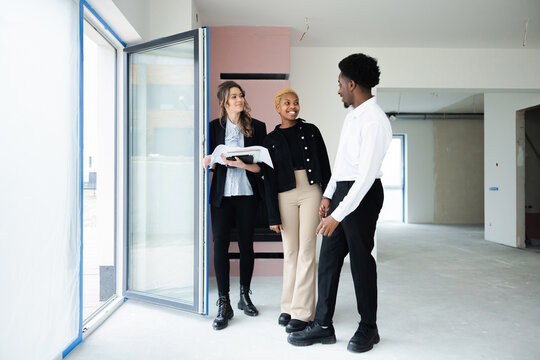Blonde real estate agent, with a warm and welcoming demeanor, points out the stunning panoramic view from the balcony, leaving the African couple in awe.