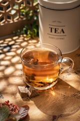 Glass cup of hot tea in bright sunlight shining into a warm cozy atmosphere, wooden table, text space