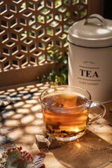 Glass cup of hot tea in bright sunlight shining into a warm atmosphere, wooden table, text space
