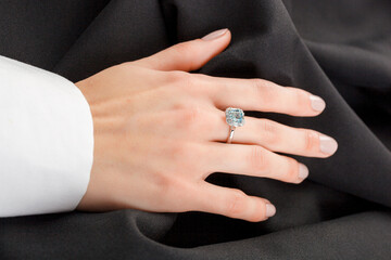 Beautiful female hand with gold ring with diamonds and emerald on gray background
