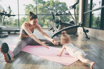 Parenthood and sport lifestyle. Young mother doing yoga with baby girl in gym. - obrazy, fototapety, plakaty