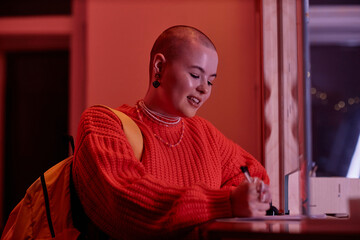 Side view portrait of smiling young woman signing in to hostel in neon lights