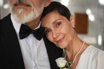Close up portrait of beautiful senior woman as bride laying head on grooms shoulder and smiling at...