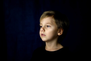 A concise portrait of a European boy. Portrait on a dark background.