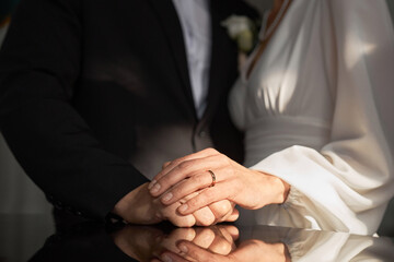 Close up of married senior couple holding hands in church with focus on wedding rings in sunlight