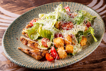Caesar salad with croutons, cheese, eggs, tomatoes and grilled chicken on wooden table