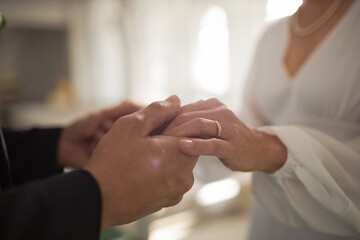 Closeup of mature bride and groom holding hands with focus on golden wedding rings, copy space