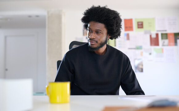 Black worker sitting in his desk at office looking thoughtful at computer screen