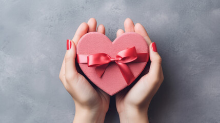 Close up top view of female hands holding a gift in a pink heart shape for valentine's day - obrazy, fototapety, plakaty