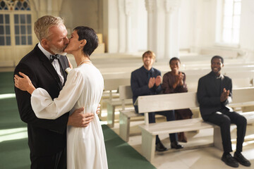 Side view portrait of loving senior couple in first kiss in church on wedding day, copy space